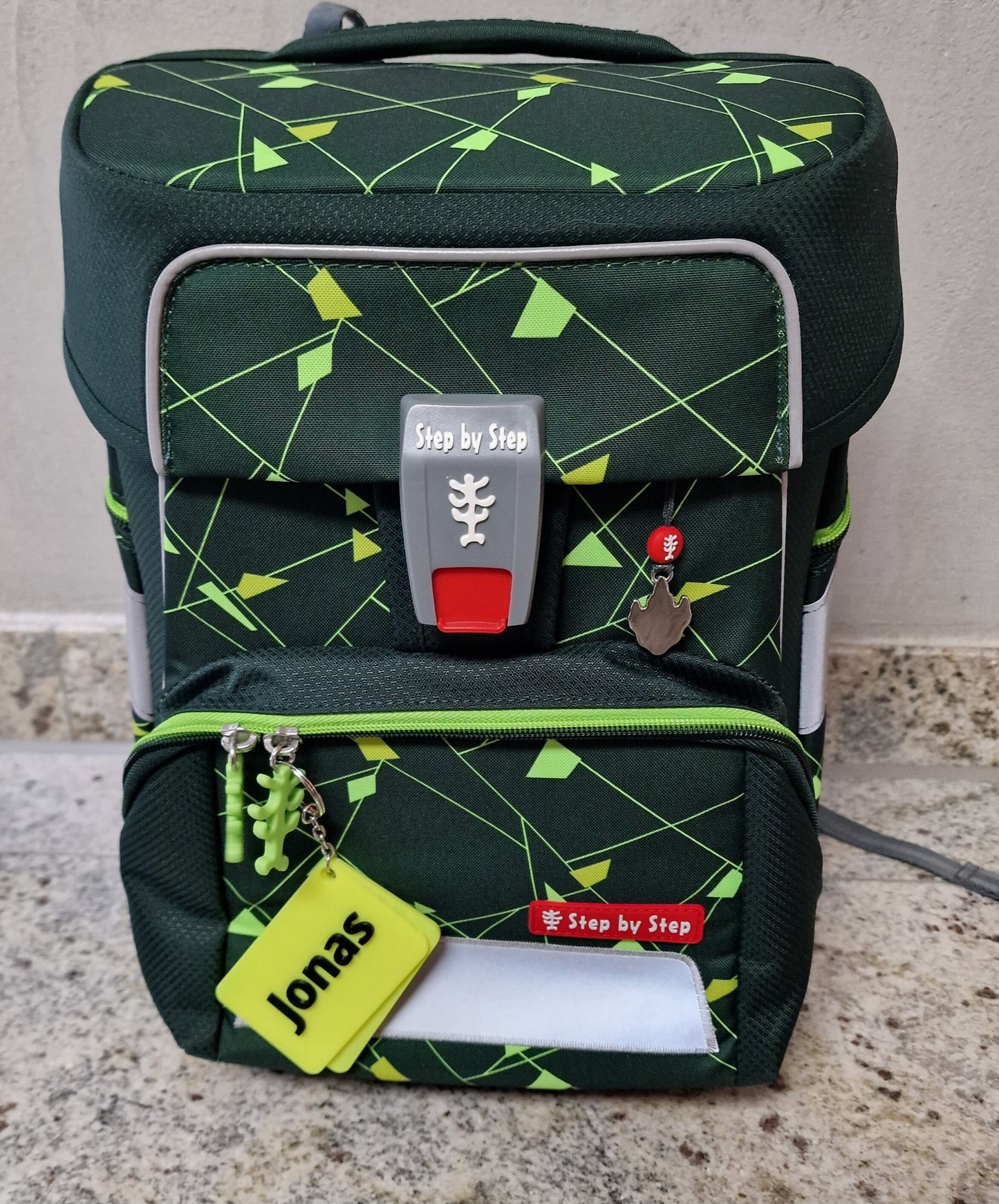 Personalisierter Anhänger mit Namen an einem Schulranzen in grün und schwarz mit geometrischem Design.