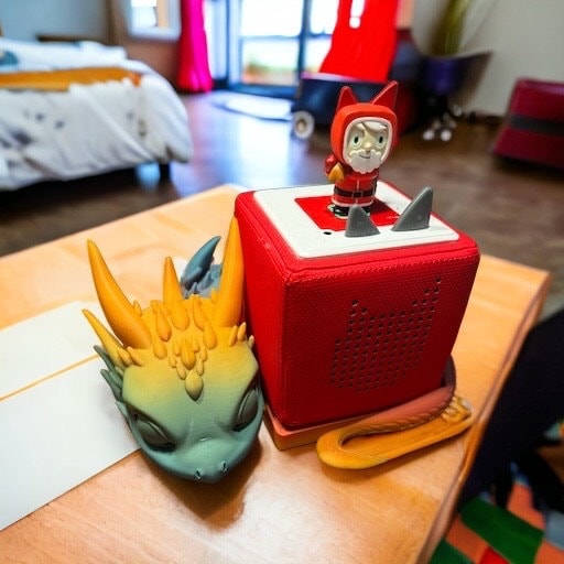 Toniebox Ständer Drachenbaby mit einem bunten Drachen und einem Tonie-Figur auf einem Tisch im Kinderzimmer.