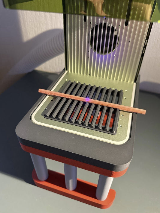 xTool F1 Jigs Set image featuring a laser engraver with a wooden stick on the grill surface.